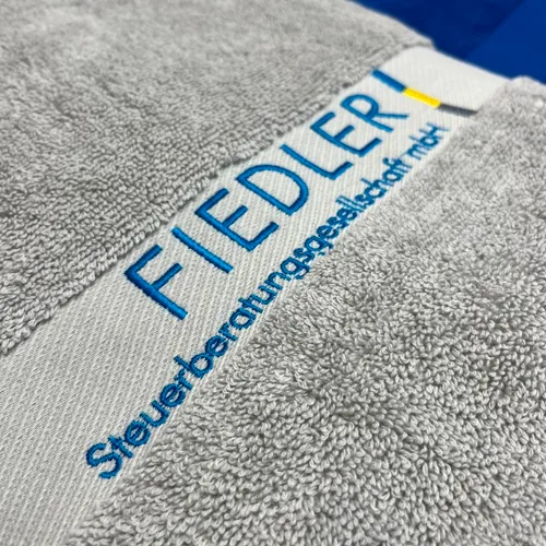 Saunatücher mit Logo besticken graues Saunatuch mit Firmenlogo bestickt in blau, gelb, grau sehr fein